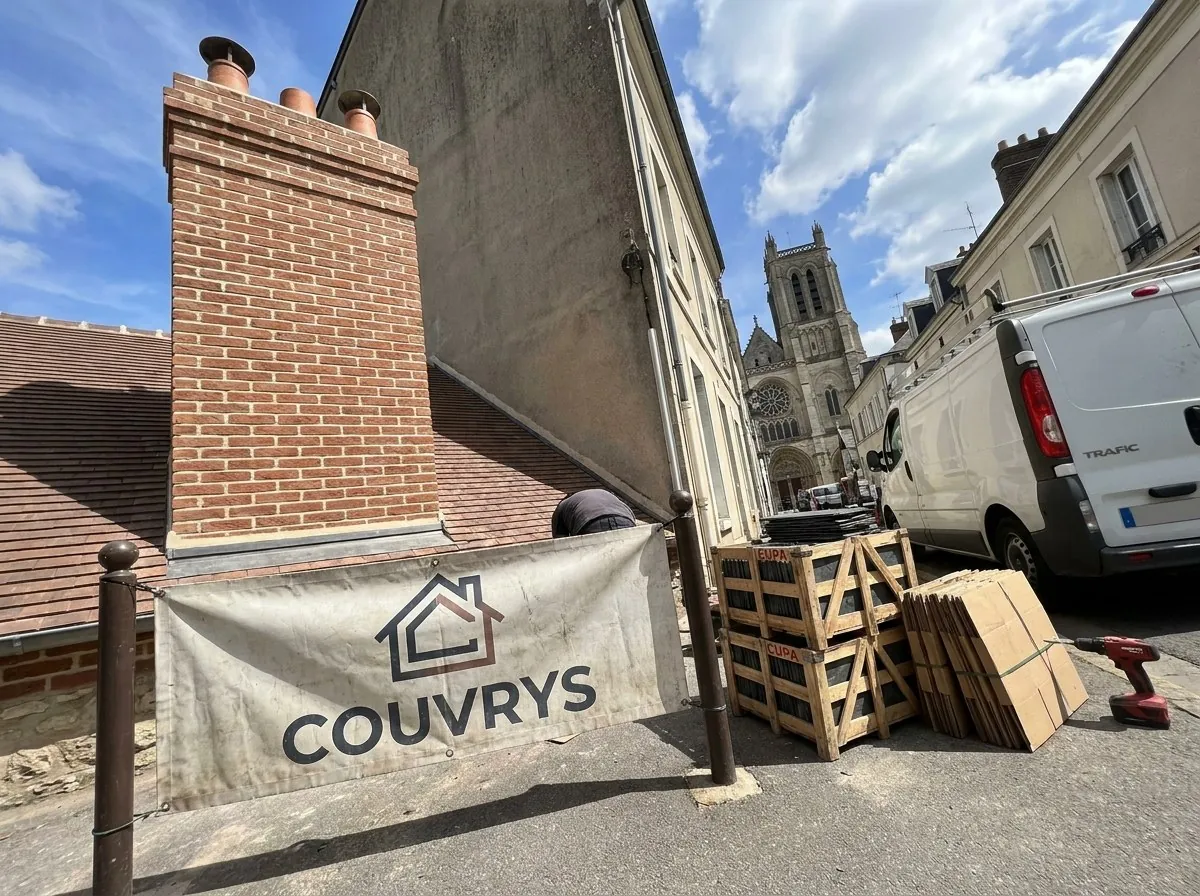 Souche de cheminée en brique remontée par Couvrys à Mantes-la-Jolie, bâche Couvrys et collégiale au bout de la rue